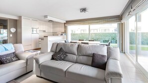Una sala de estar moderna con sofá y una mesa de centro, un área de cocina y grandes puertas corredizas de vidrio que dan a un balcón.