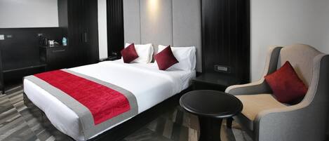 Een hotelkamer met een bed, een stoel, een tafeltje en een minibar.
