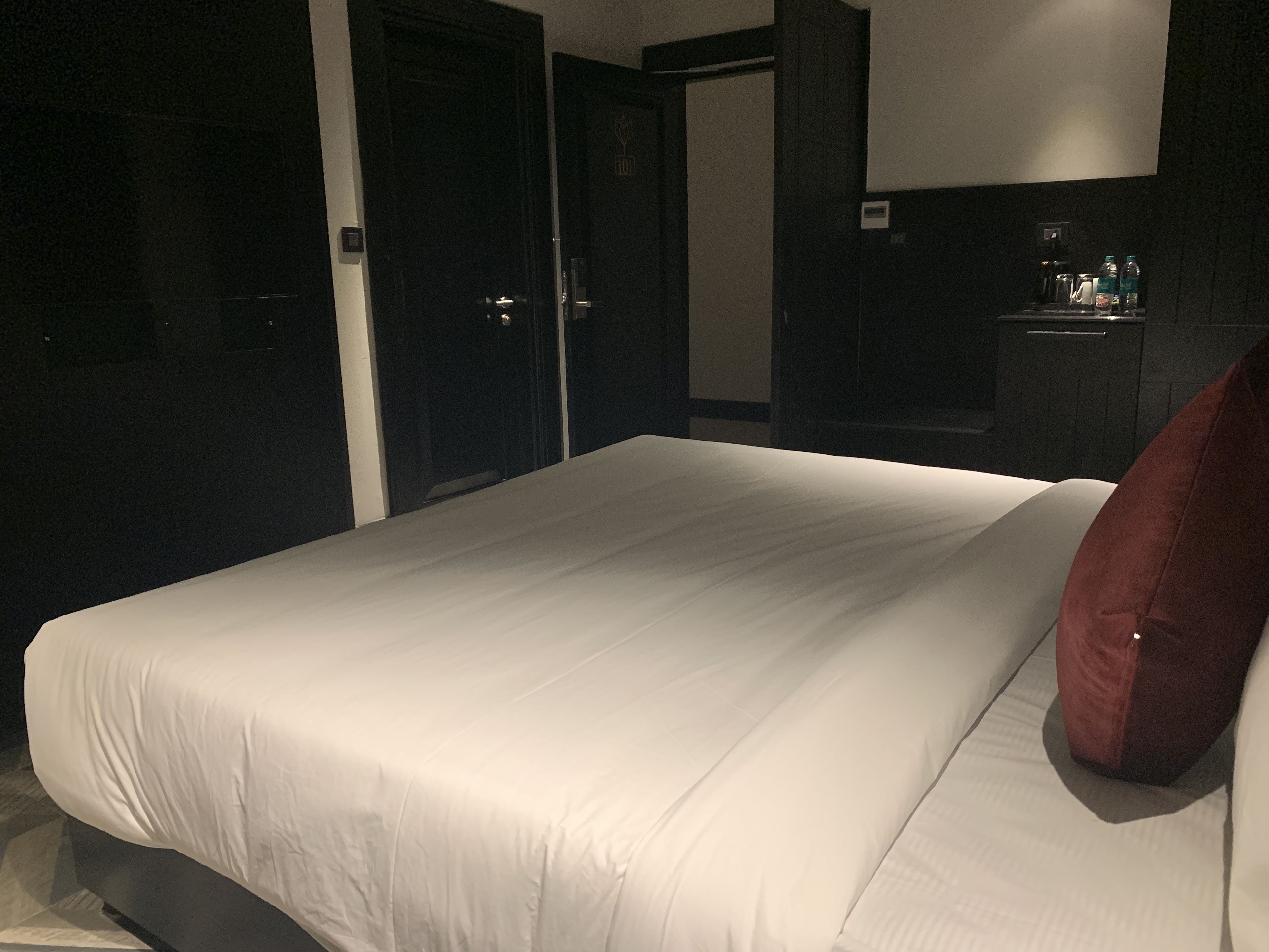 Ein Hotelzimmer mit einem großen Bett, einem roten Kissen, einer Minibar und einem dunklen Holzschrank.