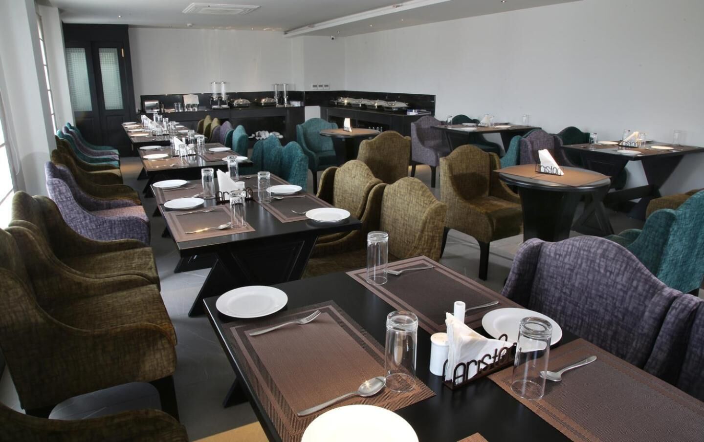 A conference room with multiple tables and chairs, equipped with name placards, and a buffet area in the background.