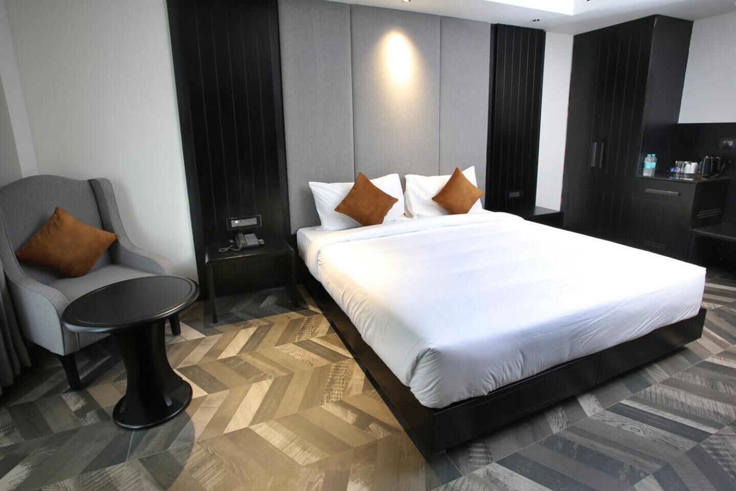 A hotel room with a large bed, a chair, a small table, and a desk with a phone.