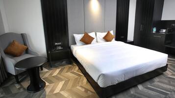 A hotel room with a large bed, a chair, a small table, and a desk with a phone.