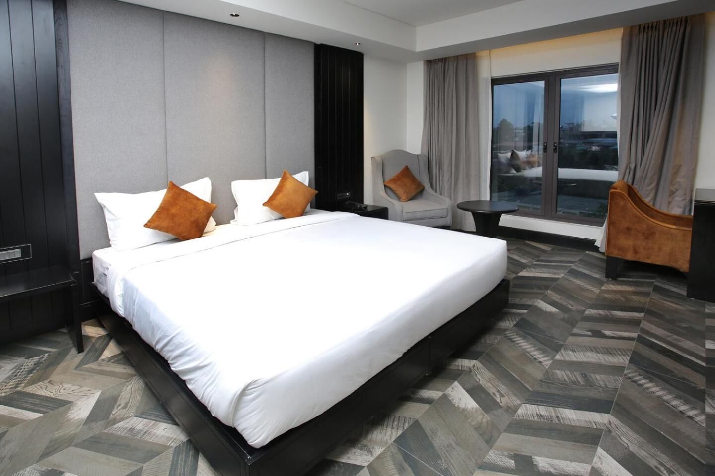 Une chambre d’hôtel moderne dotée d’un grand lit, d’un coin salon et offrant une vue sur la ville grâce à de grandes fenêtres.