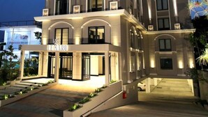Un hotel a più piani con un design architettonico classico, caratterizzato da un ingresso in evidenza con tenda e una facciata ben illuminata.