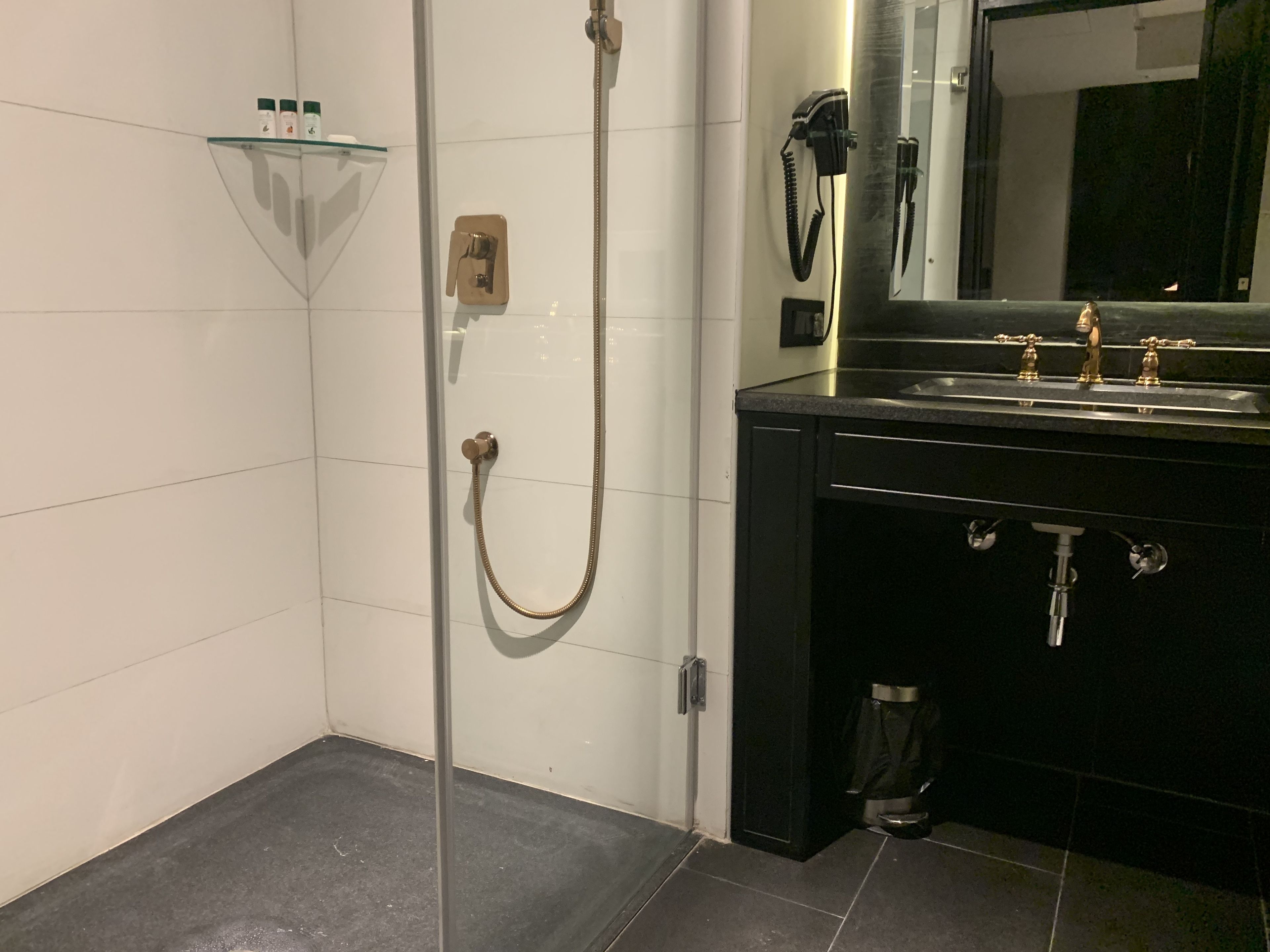Un baño moderno con cabina de ducha de vidrio, un lavabo negro con detalles dorados y un espejo sobre el lavabo.