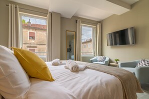 Una habitación de hotel con cama, dos sillones, un televisor y una ventana con cortinas.
