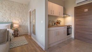 A compact living space with a kitchenette, a bed with a headboard, a small bedside table with a lamp, and a patterned rug. - Luxurious Suites Elegance (Zadar)