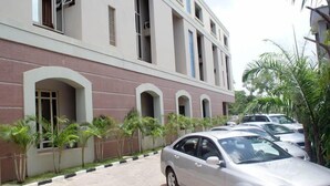 A building with a row of parked cars and a paved driveway. - Marvel Hotel  Suites (Abuja)