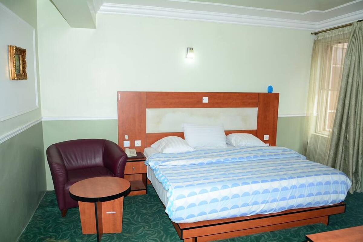 A hotel room with a wooden bed, a small round table, a leather chair, and a nightstand with a lamp.