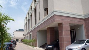 A building with a covered entrance, a parking area with several cars, and a clear sky. - Marvel Hotel  Suites (Abuja)