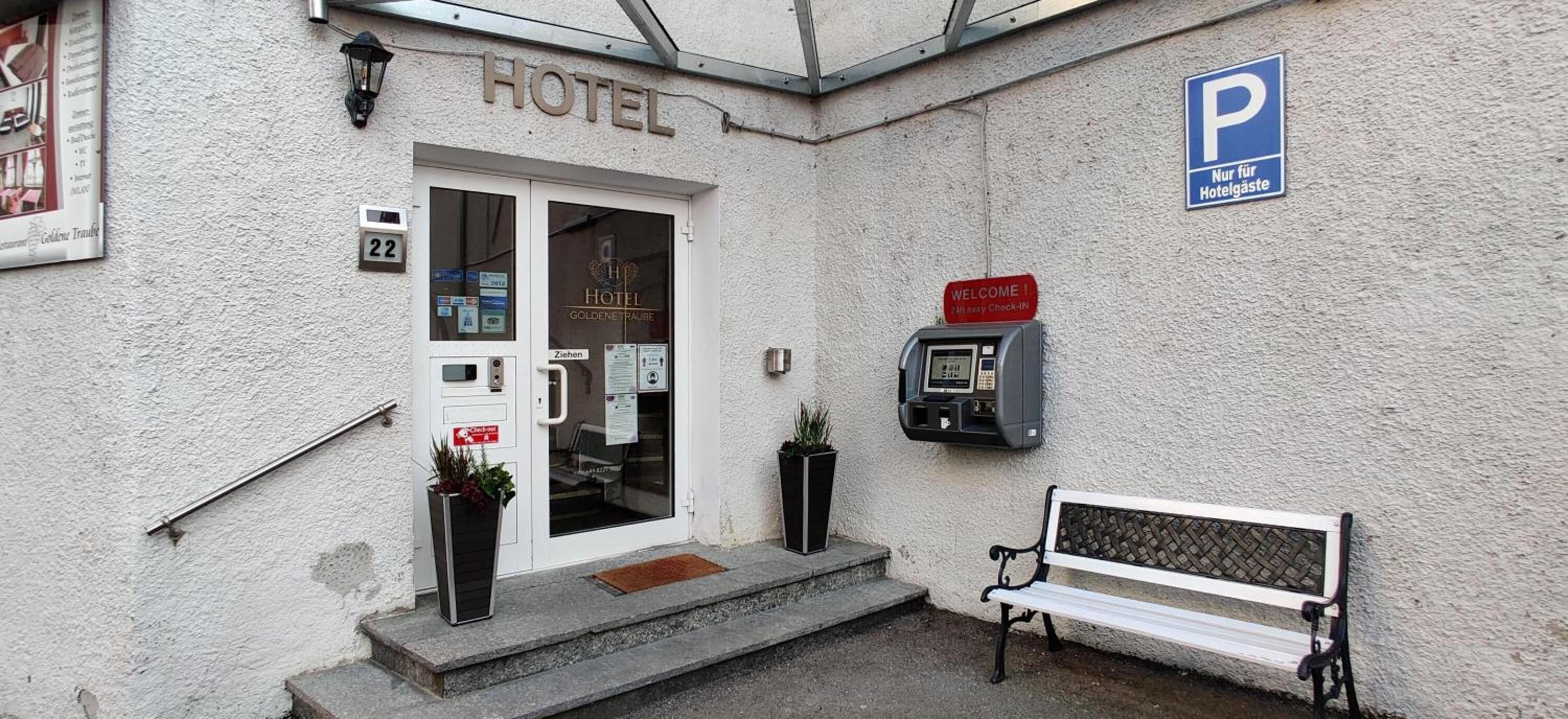 A hotel entrance with a sign reading "HOTEL," a parking sign, a welcome sign, and a payment machine.