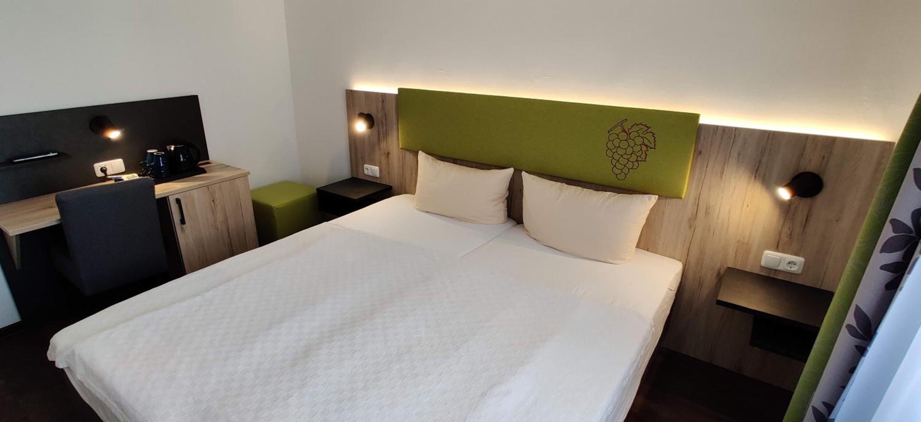 A hotel room with a bed, a desk, and a chair. There are two bedside tables with lamps.