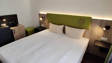 Ein Hotelzimmer mit einem Bett, einem Schreibtisch und einem Sessel. Es gibt zwei Nachttische mit Lampen.