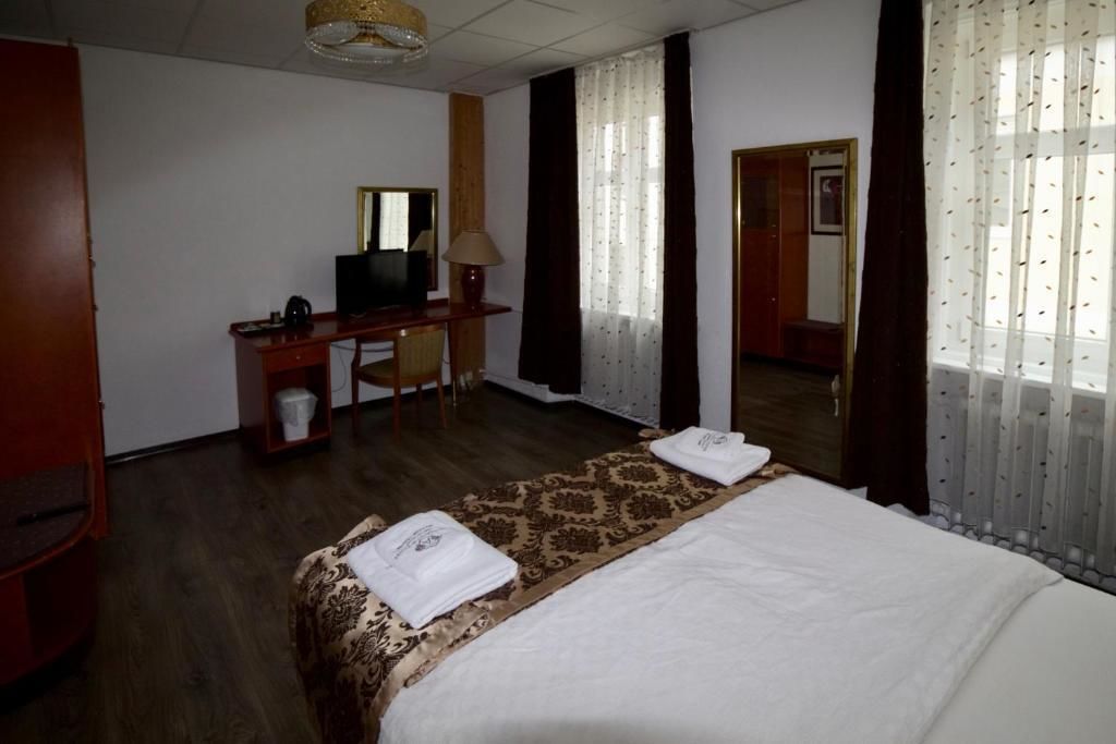 A hotel room with a bed, a desk, a chair, a lamp, and a mirror.