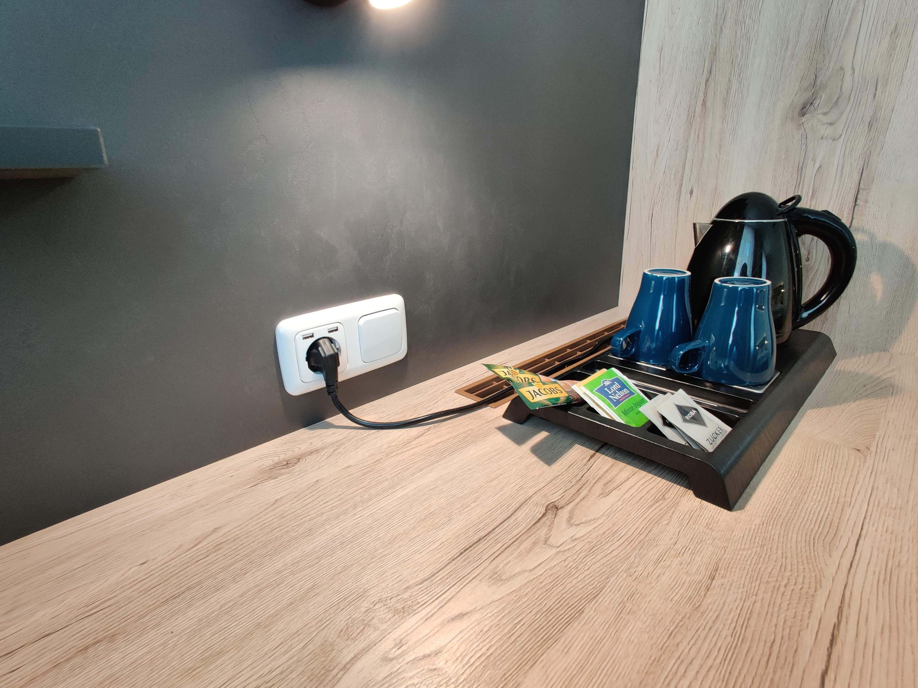 Eine Holzausziehtisch mit einer Kaffeemaschine, blauen Tassen und einer Schale mit Kaffeekapseln.