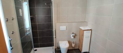 Un baño con ducha, inodoro y un pequeño armario de madera.