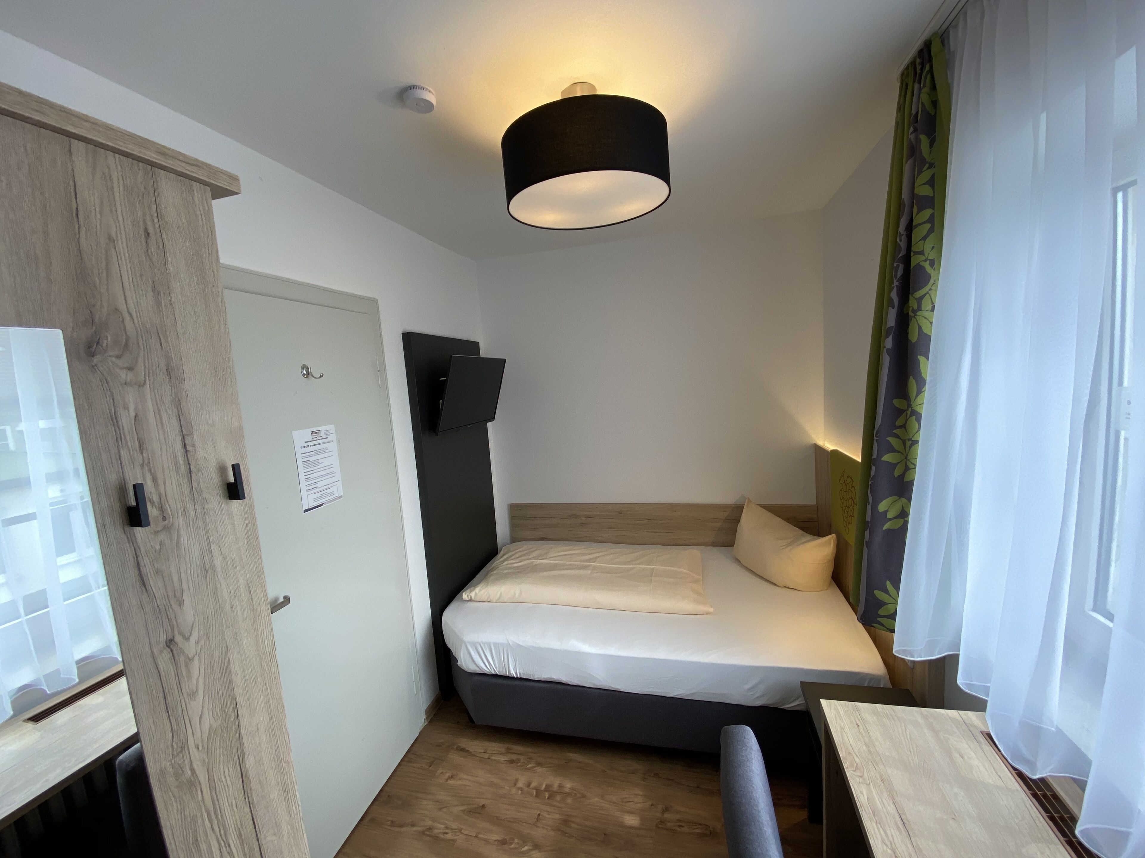 A small, modern room with a bed, a desk, and a mounted TV.