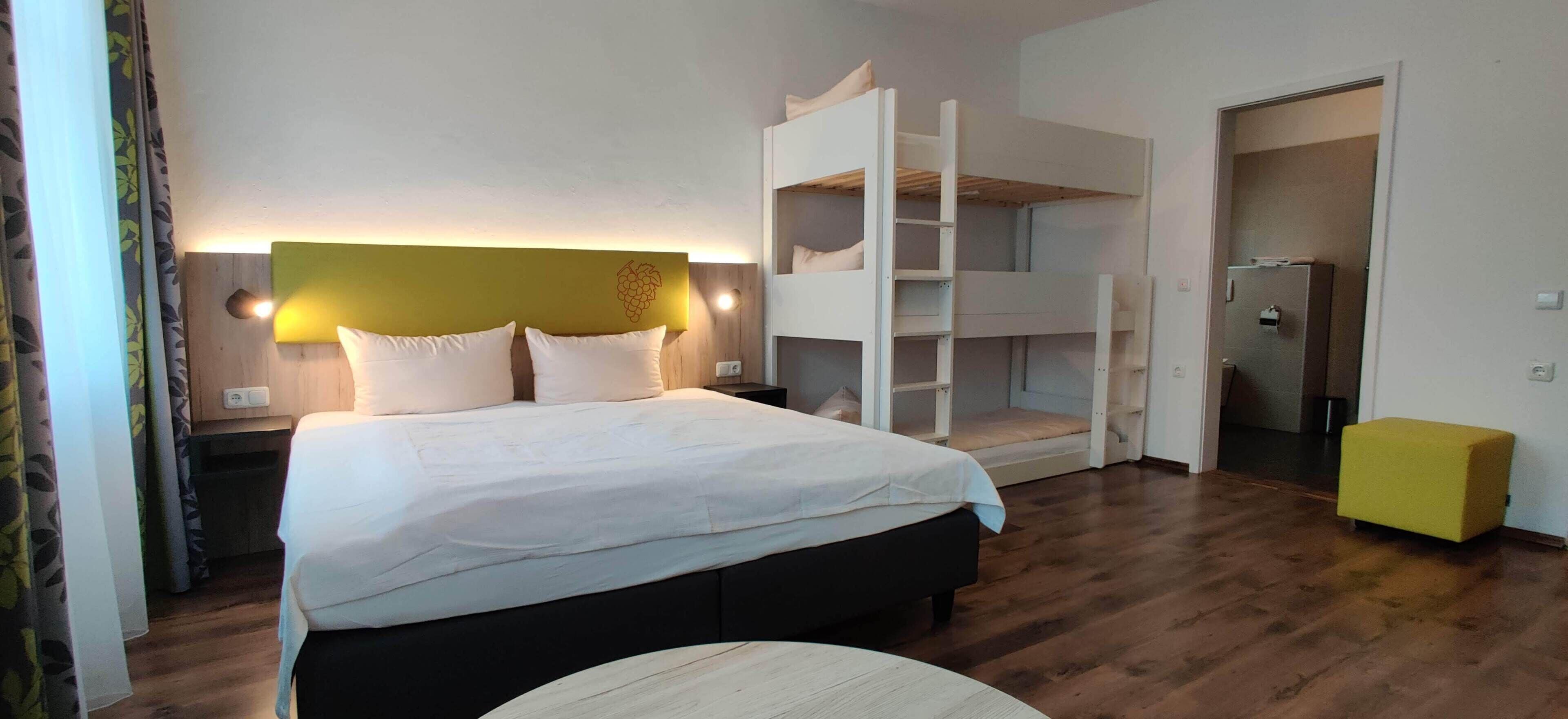 Habitación de hotel con cama, suelo de madera, cabecera blanca y pared amarilla, además de una puerta.