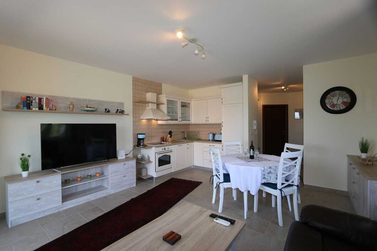 Een moderne keuken met witte kastjes, een inbouwoven en een eethoek met een tafel en stoelen.