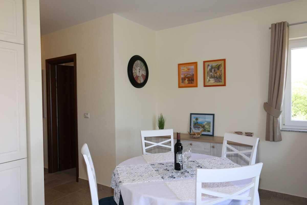 A dining area with a round table, white chairs, a clock, and two framed pictures on the wall.