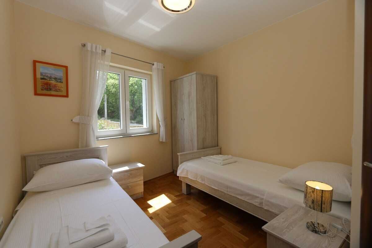 A bedroom with two beds, a wardrobe, a window with curtains, and a bedside lamp.