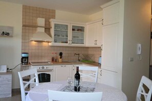 Cocina compacta con armarios blancos, estufa a gas, cafetera y mesa de comedor con sillas.