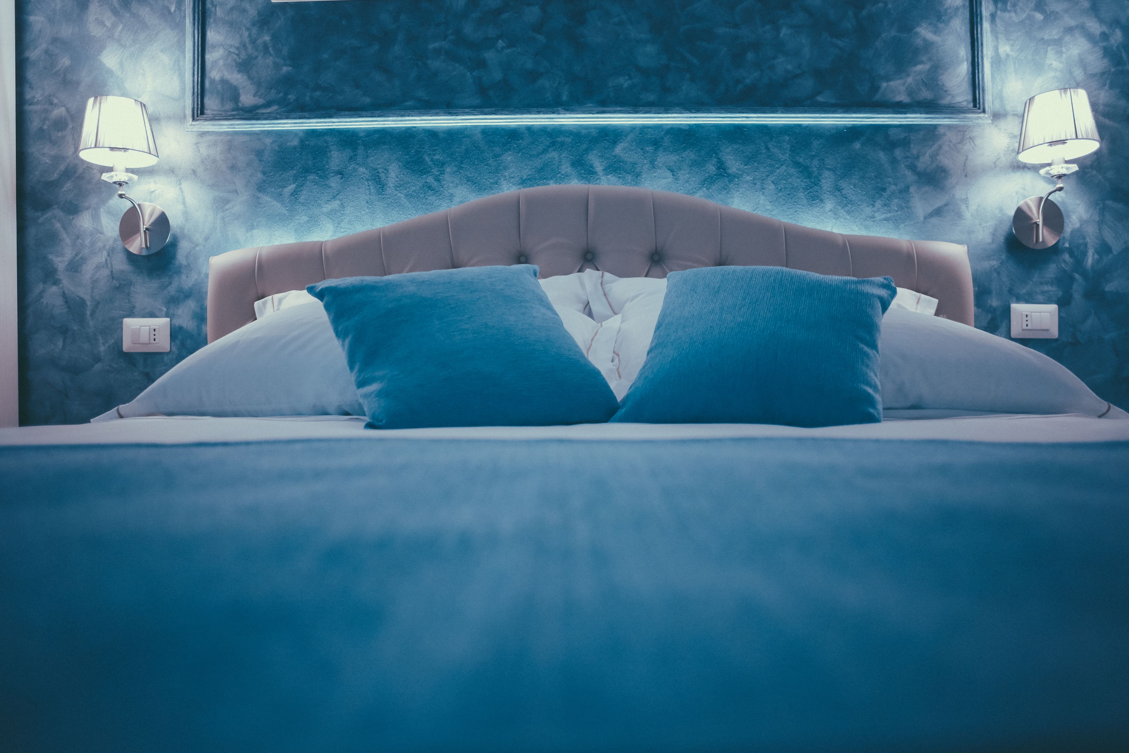 A bed with a tufted headboard, two wall-mounted lamps, and a textured wall behind it.