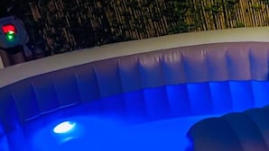 Un jacuzzi con luz azul, escalones de piedra y estructura de madera.