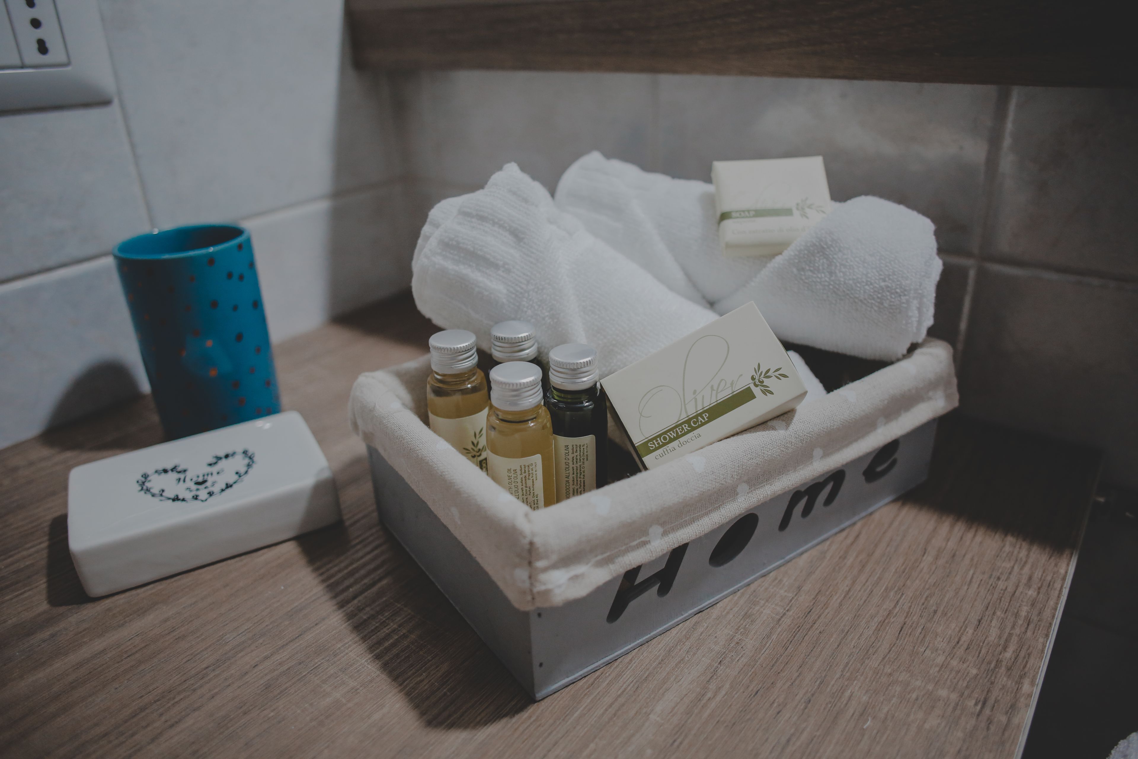 A bathroom with a wooden vanity, a blue cup, and a metal container labeled "Home" holding toiletries.