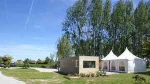 A small wooden cabin with a garden in front, a white tent to the right, and a clear blue sky. - Les Gites De Montmartre (Le Perrier)