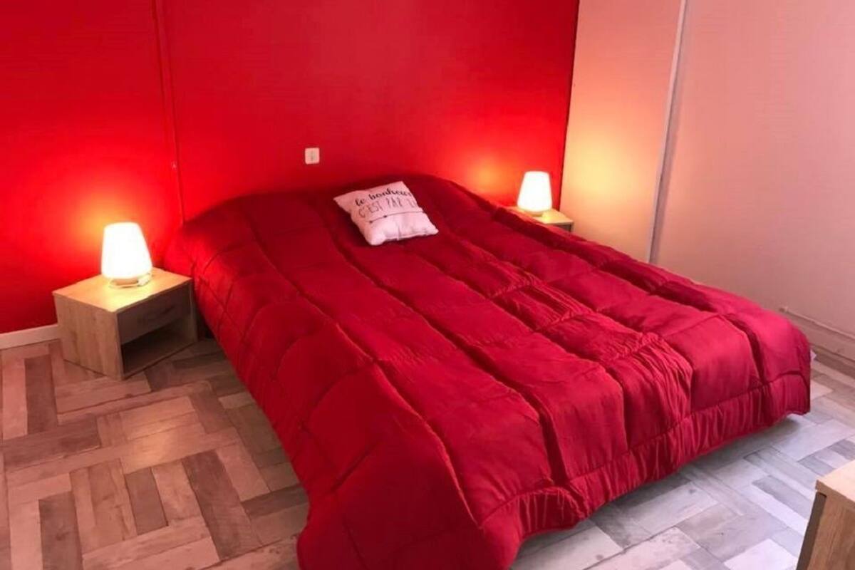 Uma cama com um cobertor vermelho e duas luminárias de cabeceira.