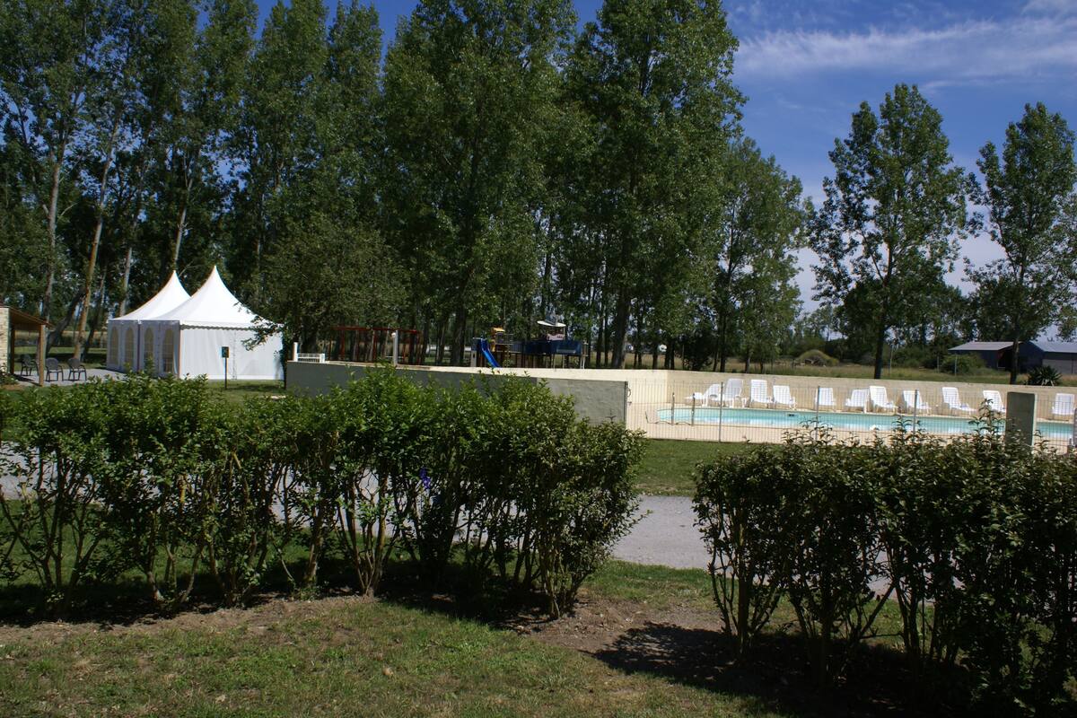 Uma área de piscina com espreguiçadeiras, uma tenda branca e árvores ao fundo.
