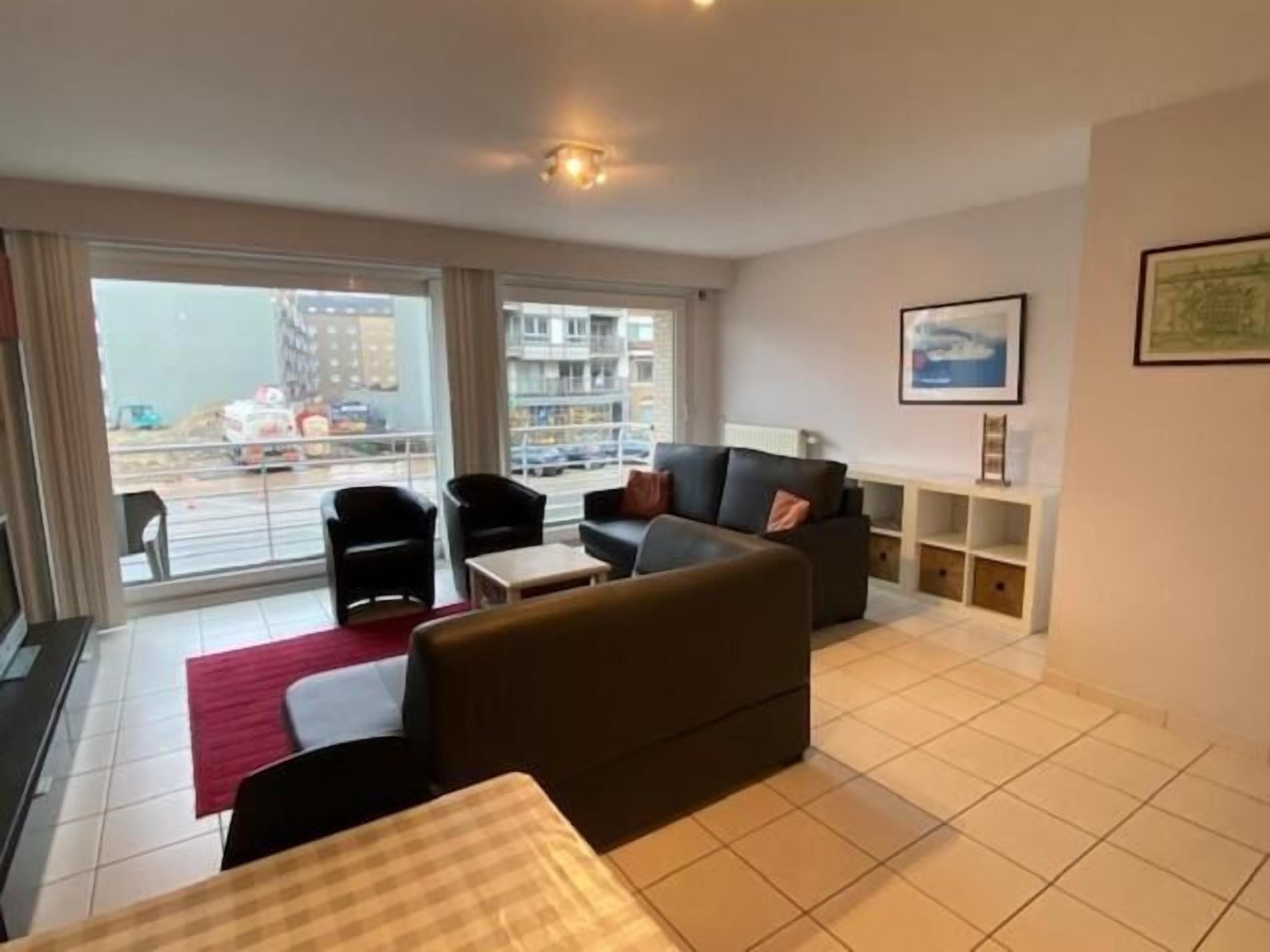 A modern living room with a sofa, chairs, a small table, and a balcony with a view of the city.