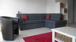 A modern living room with a grey sectional sofa, a red rug, and a white coffee table. - Kompas 1 0102 (Nieuwpoort)
