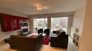A modern living room with a grey sofa, a TV, and a red cabinet. - Kompas 1 0102 (Nieuwpoort)