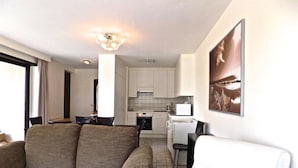 A modern living room with a sofa and a chair, a dining area with a table and chairs, a kitchen with white cabinets, and a large framed picture on the wall. - Havenzicht 105 (Nieuwpoort)
