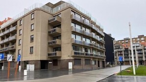 A multi-story residential building with balconies, a parking area, and a pedestrian pathway. - Havenzicht 105 (Nieuwpoort)