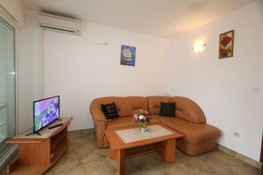 Una sala de estar con sofá, una mesa de centro, televisor sobre un mueble bajo y aire acondicionado instalado en la pared.