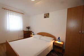 Un dormitorio con cama, mesitas de noche, escritorio, silla, armario y ventana con cortinas.