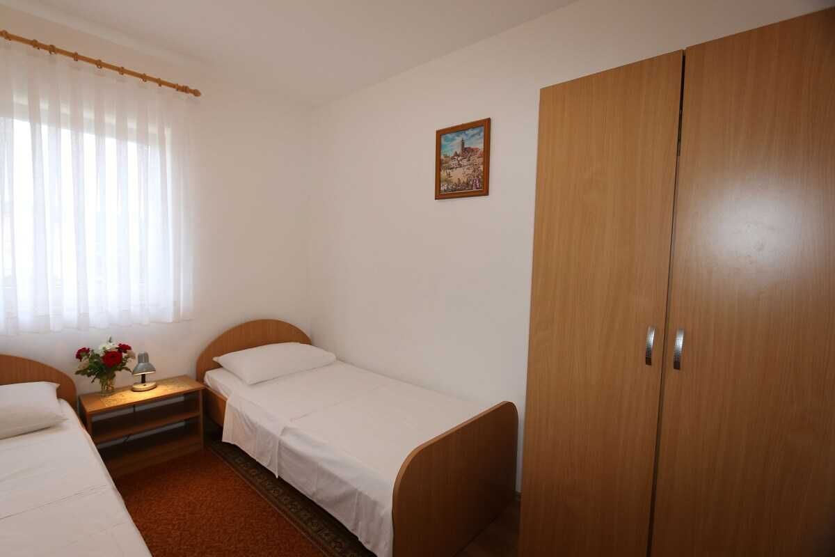 Een kamer met twee eenpersoonsbedden, een houten garderobe, een nachtkastje met een lamp en bloemen, en een schilderij aan de muur.