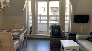 A cozy living area with a dining table, wicker chairs, a sofa, a small white table, and a television. - Noorderbries 404 (Nieuwpoort)
