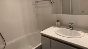 A modern bathroom with a white bathtub, a sink with a mirror above it, and a showerhead. - Noorderbries 404 (Nieuwpoort)