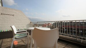 Un balcón con pared de ladrillo blanco, baranda metálica y vistas a edificios distantes.