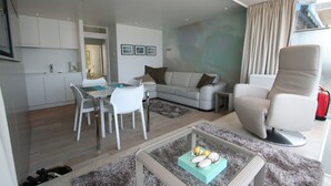 Una sala moderna con un sofá, una mesa de comedor con sillas, una mesa de centro y una zona de cocina con armarios y un ventanal.