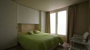 Un dormitorio con cama, una silla y una ventana.