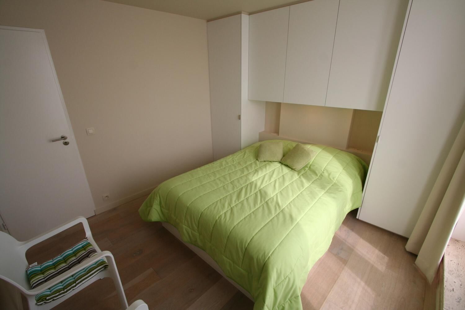 Een compacte, keurig opgeruimde slaapkamer met een bed, een kledingkast en een plank met netjes gevouwen spullen.