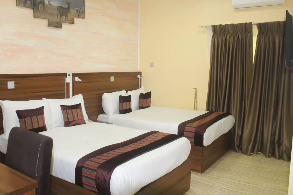 A hotel room with two beds, a wooden headboard, a painting on the wall, and a curtain.