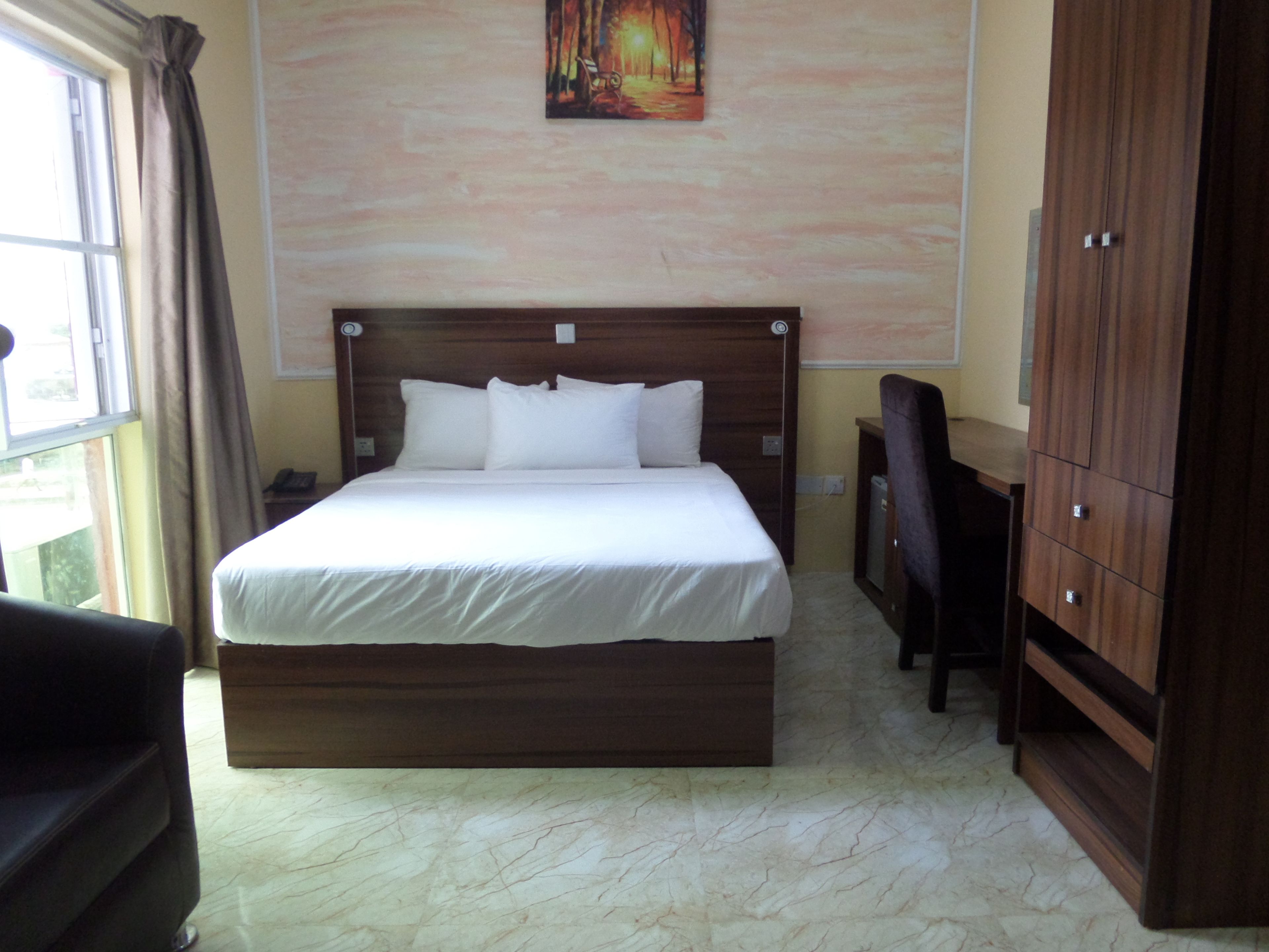 A bedroom with a large bed, a wooden headboard, a desk, and a wardrobe.