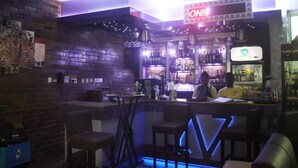 Zona de bar con un letrero de neón, paredes de ladrillo y un cantinero.