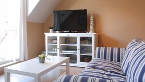 A living room with a white TV stand, a striped sofa, and a small table with a plant. - Cezanne (Nieuwpoort)